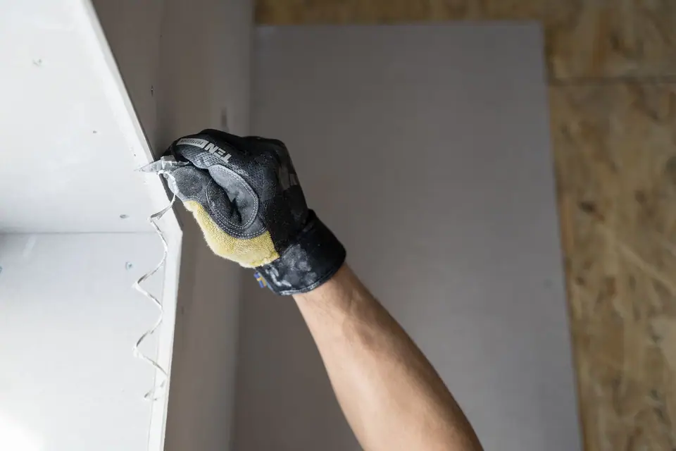 A gloved hand smoothing joint compound along a drywall corner (stock photo)