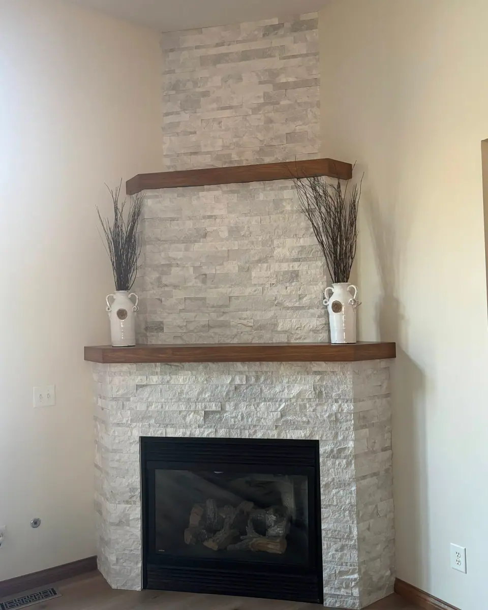 Corner fireplace in stacked stone with two wood mantel shelves, a Dream Big Contracting project