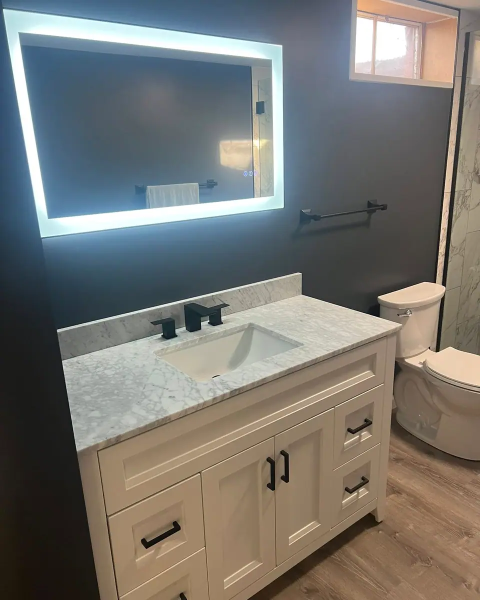 Bathroom vanity with black fixtures and hardware under a lit mirror, a Dream Big Contracting project